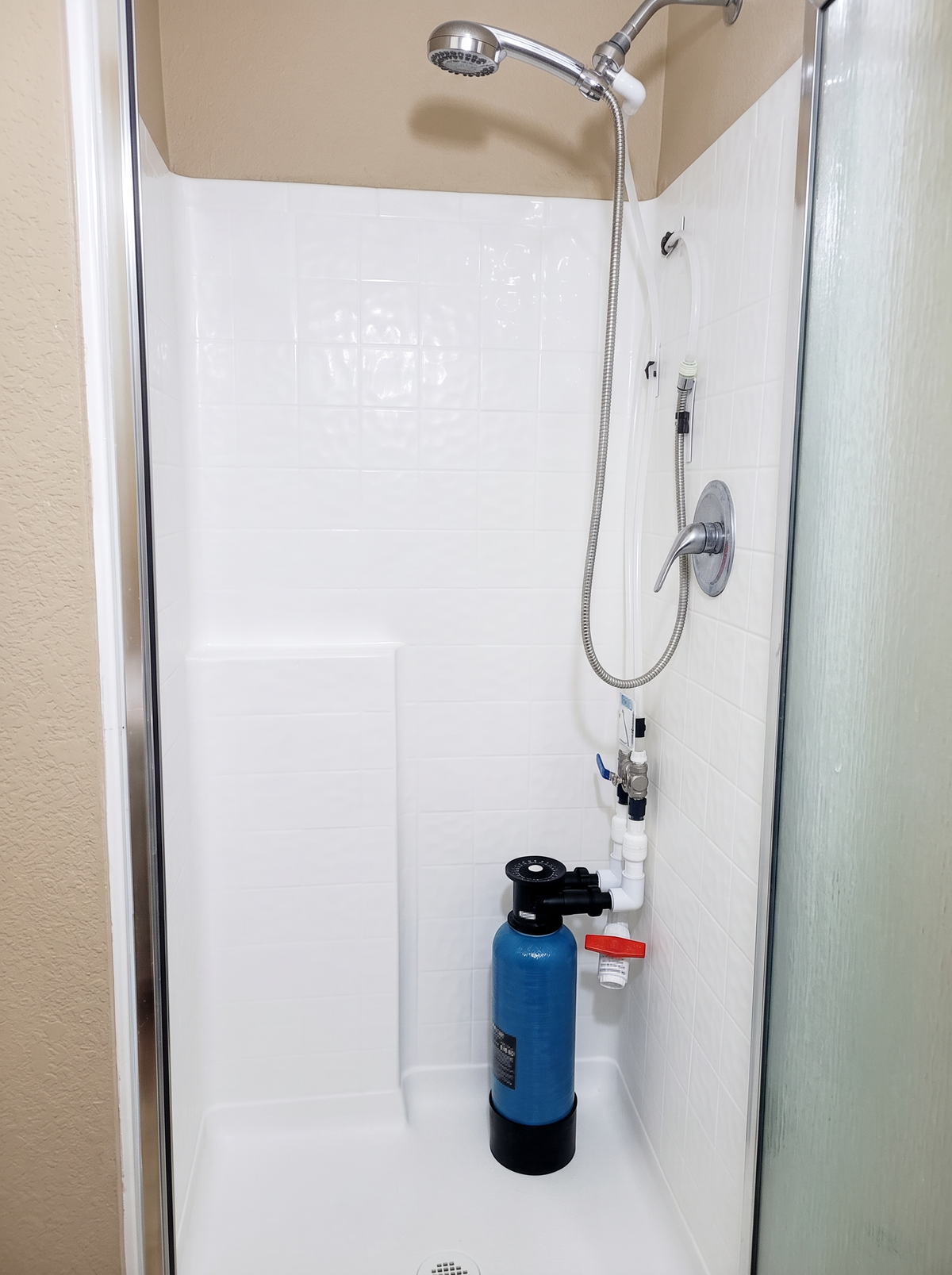 MiniMax Model I water softener tank installed inside shower with hoses connected to water supply and shower head
