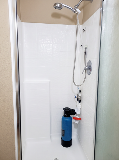 MiniMax Model I water softener tank installed inside shower with hoses connected to water supply and shower head