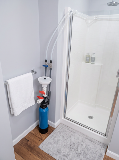 MiniMax Model O water softener tank installed outside shower with hoses connected to water supply and shower head